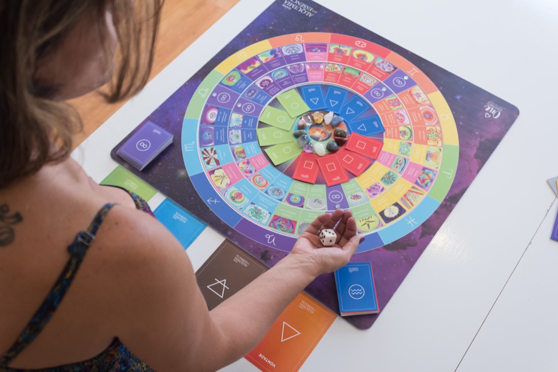 O Tabuleiro Alquimia da Essência durante uma sessão — cartas, cristais e o dado na mão